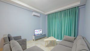 Een moderne woonkamer met een grijze modulaire bank, een klein wit bijzettafeltje en een flatscreen televisie op een grijze kast.