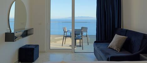 Quarto de hotel moderno com varanda, sofá, poltrona e um espelho grande.