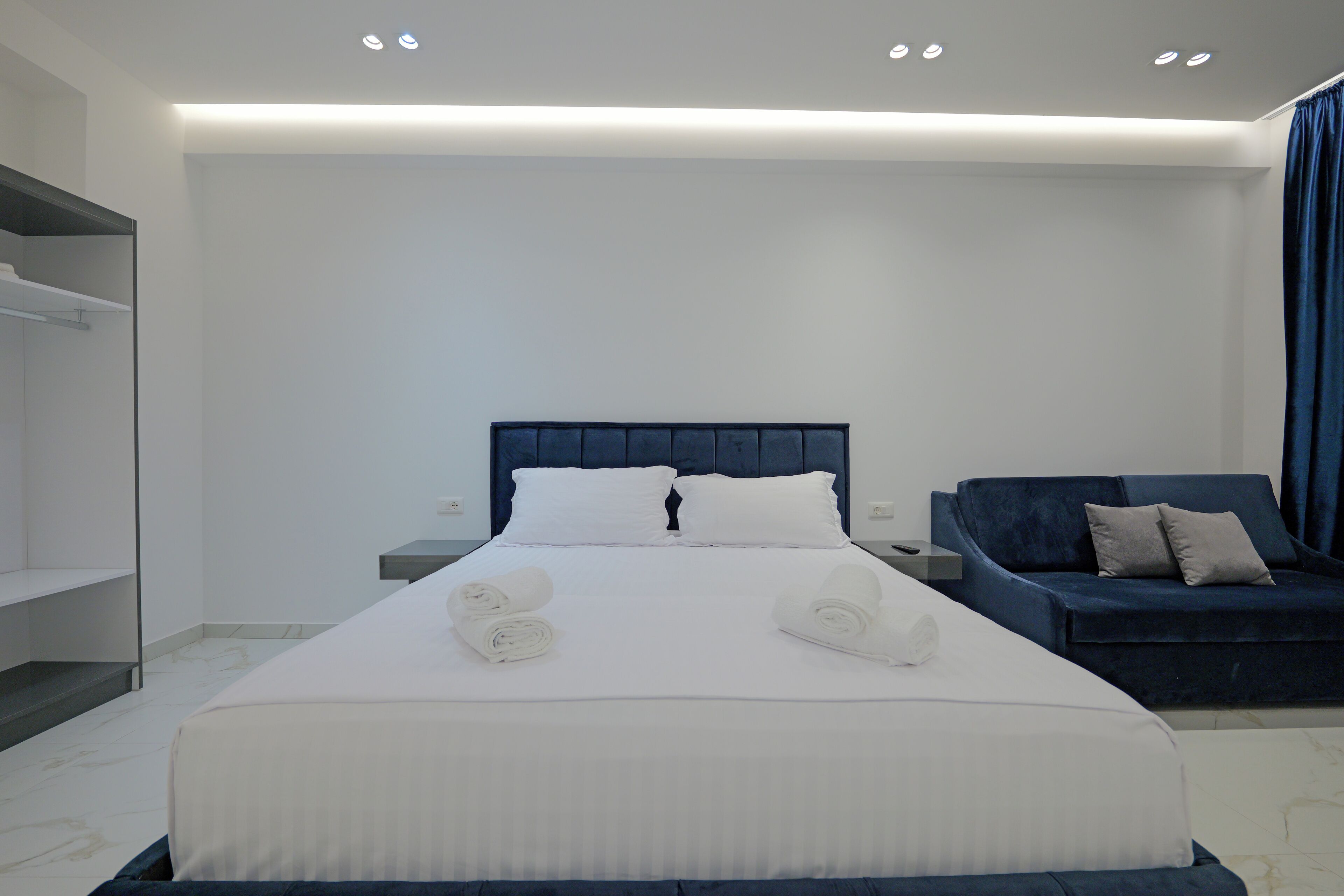 A modern hotel room with a large bed, a dark blue headboard, and a blue sofa.