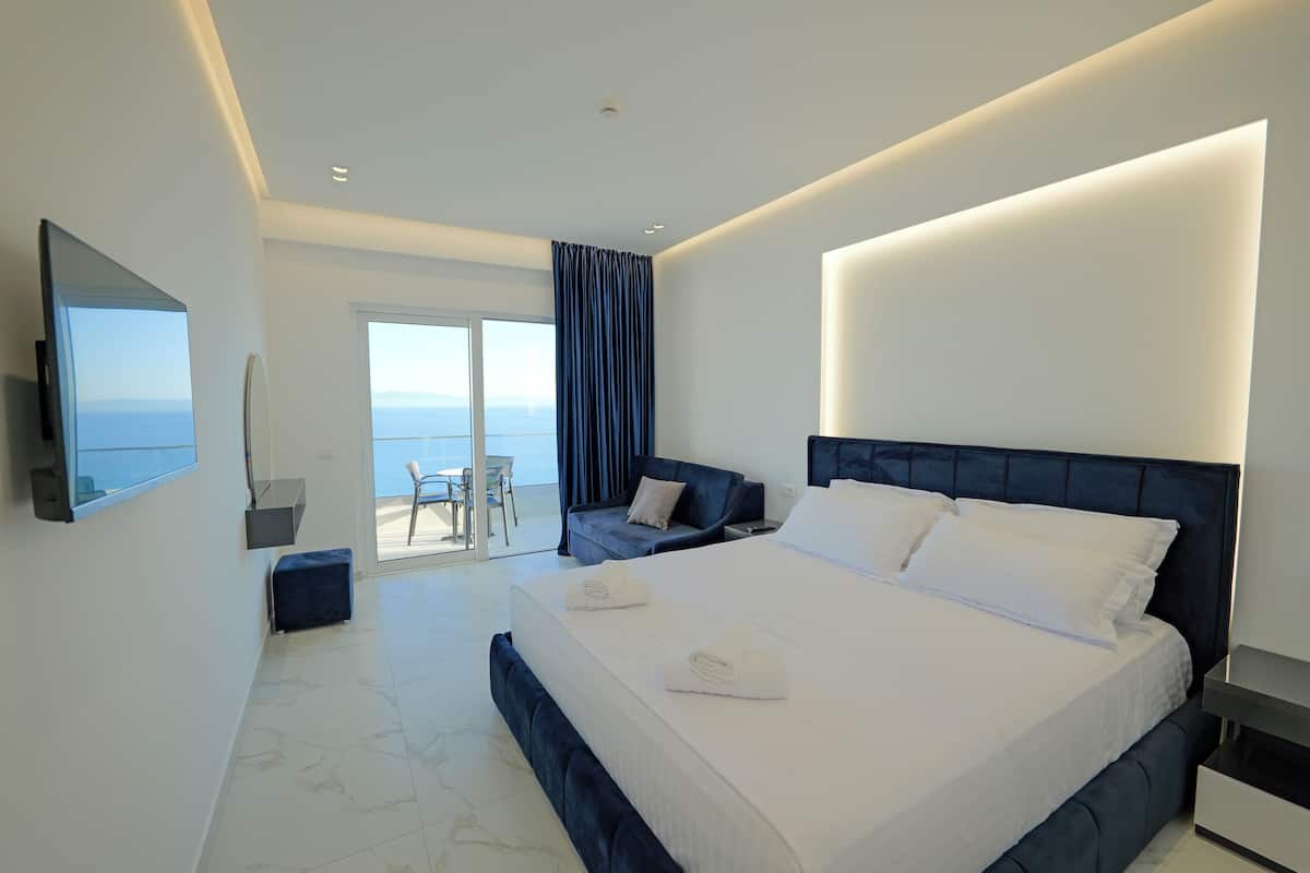 Una habitación de hotel moderna con una cama grande, televisión de pantalla plana, balcón con vistas y zona de comedor.