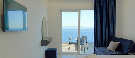 Una habitación de hotel moderna con una cama, un televisor, un pequeño reposapiés, un sofá y un balcón con vistas al mar.