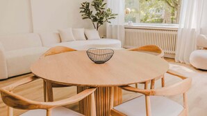 Un espace repas moderne avec une table ronde en bois, six chaises et un luminaire suspendu.