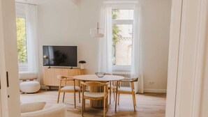 Un vaste espace de vie doté d’un plancher en bois, d’une table de salle à manger ronde et d’un téléviseur posé sur un meuble en bois.