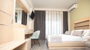 Una habitación de hotel moderna con una cama, un escritorio, una silla, un televisor y un equipo de aire acondicionado.