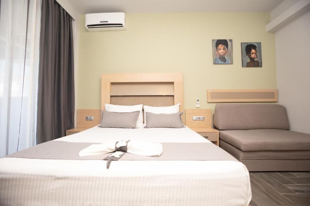 A hotel room with a large bed, a bedside table, an air conditioning unit, and two wall-mounted paintings.