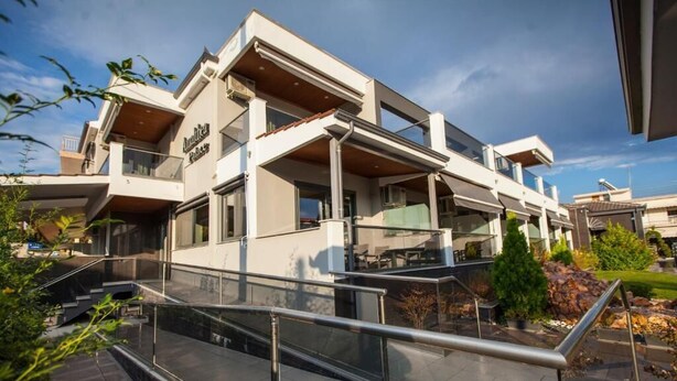 Un edificio moderno de varios pisos con techo plano, ventanas grandes y un área exterior cubierta con asientos.