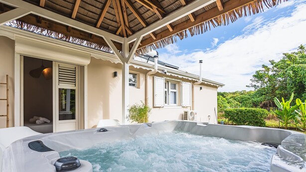 A hot tub with a wooden pergola overhead, a white exterior wall, and a view of lush greenery. - Villa Sugar Cane: Pool and Jacuzzi (Le Moule)