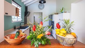 A kitchen with a wooden table, a bowl of fruits, a vase of flowers, and a clock on the wall. - Villa Sugar Cane: Pool and Jacuzzi (Le Moule)