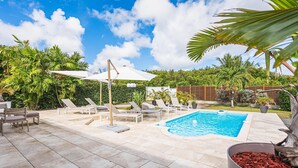A backyard with a swimming pool, lounge chairs, and a pergola with an umbrella. - Villa Sugar Cane: Pool and Jacuzzi (Le Moule)