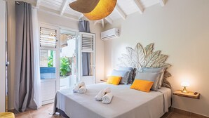 A bedroom with a bed, curtains, a window, and a bedside table with a lamp. - Villa Sugar Cane: Pool and Jacuzzi (Le Moule)