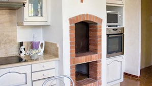 A kitchen with a built-in brick oven, white cabinetry, and a marble countertop.