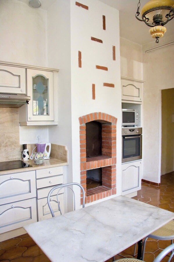 A kitchen with a built-in brick oven, white cabinetry, and a marble countertop.
