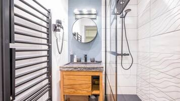 Une salle de bain avec un meuble-lavabo en bois, un miroir rond avec éclairage intégré, un espace douche et un mur carrelé.