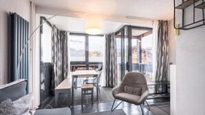 Un salon moderne avec un canapé, un fauteuil, une table à manger et une vue dégagée grâce à de grandes fenêtres.