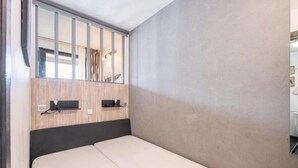 Une chambre à coucher avec un lit, une tête de lit en bois, un miroir et une petite étagère sur laquelle se trouve une lampe.