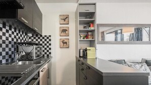 Une cuisine compacte avec un crédence à carreaux, un four encastré et un petit îlot central doté d’un évier.