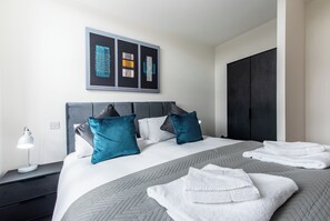 A hotel room with a large bed, two pillows, a bedside lamp, and a framed artwork above the bed. - The Glassworks (Nottingham)