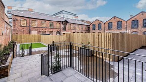 A courtyard with a wooden fence, a small lawn, and a brick building with multiple windows. - The Glassworks (Nottingham)