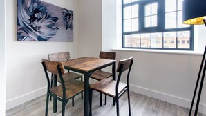 A dining area with a wooden table and chairs, a large abstract painting on the wall, and a window with a view of buildings outside. - The Glassworks (Nottingham)