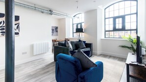 A modern living room with a blue sofa, a dining area with a table and chairs, and large windows providing natural light. - The Glassworks (Nottingham)