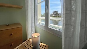 Une pièce avec une fenêtre, une commode en bois et une table sur laquelle se trouve une bougie.