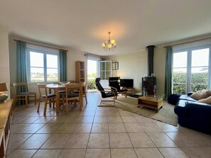 A living room with a dining area, a fireplace, and large windows. - Les pieds dans l eau Home - Waterfront Stay (Barfleur)