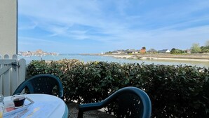 Un balcon avec une table et des chaises, donnant sur une zone côtière avec des bâtiments et un phare.