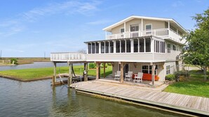 Een herenhuis met twee verdiepingen aan het water, met een overdekt terras en een zitgedeelte buiten.