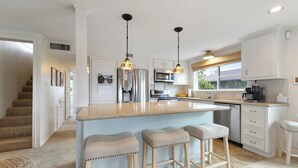 Een moderne keuken met een centraal kookeiland, roestvrijstalen apparatuur en hangende lampen.