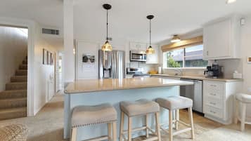 Une cuisine moderne dotée d’un îlot central, d’appareils électroménagers en acier inoxydable et de luminaires suspendus.