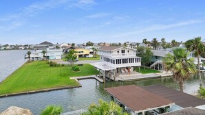 Een pand aan het water met een steiger, een gazon en een twee verdiepingen tellend huis met een balkon.