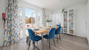 A dining area with a wooden table, blue chairs, and a white cabinet with glass doors. - Stylish 3-Bed Retreat with Hot Tub & Garden | Near Perth City Centre (Perth)