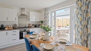 A modern kitchen with white cabinets, a built-in stove, and a dining area with a wooden table set for four. - Stylish 3-Bed Retreat with Hot Tub & Garden | Near Perth City Centre (Perth)