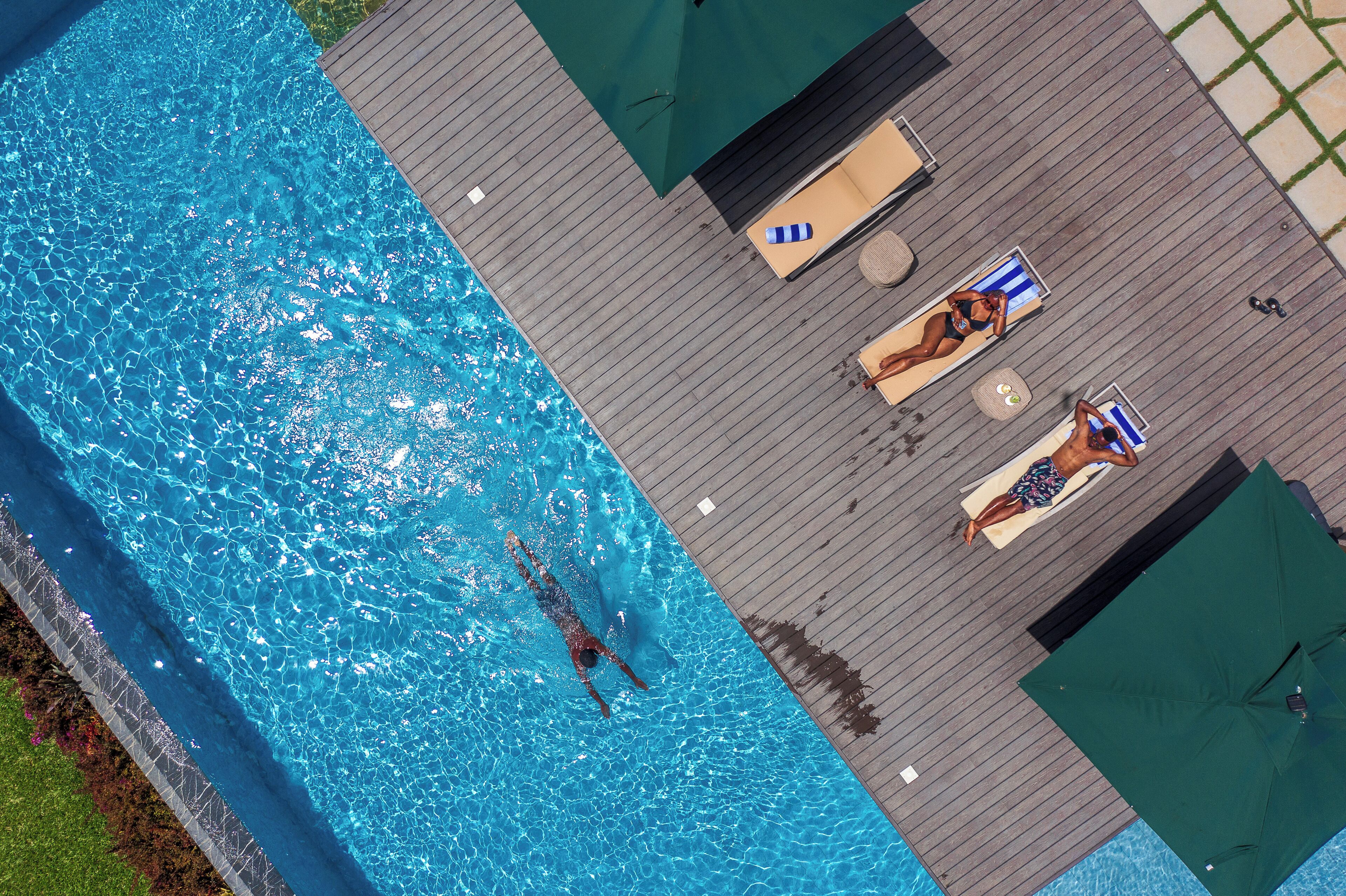 Vue aérienne d’une piscine avec une terrasse en bois, des chaises longues et des parasols.