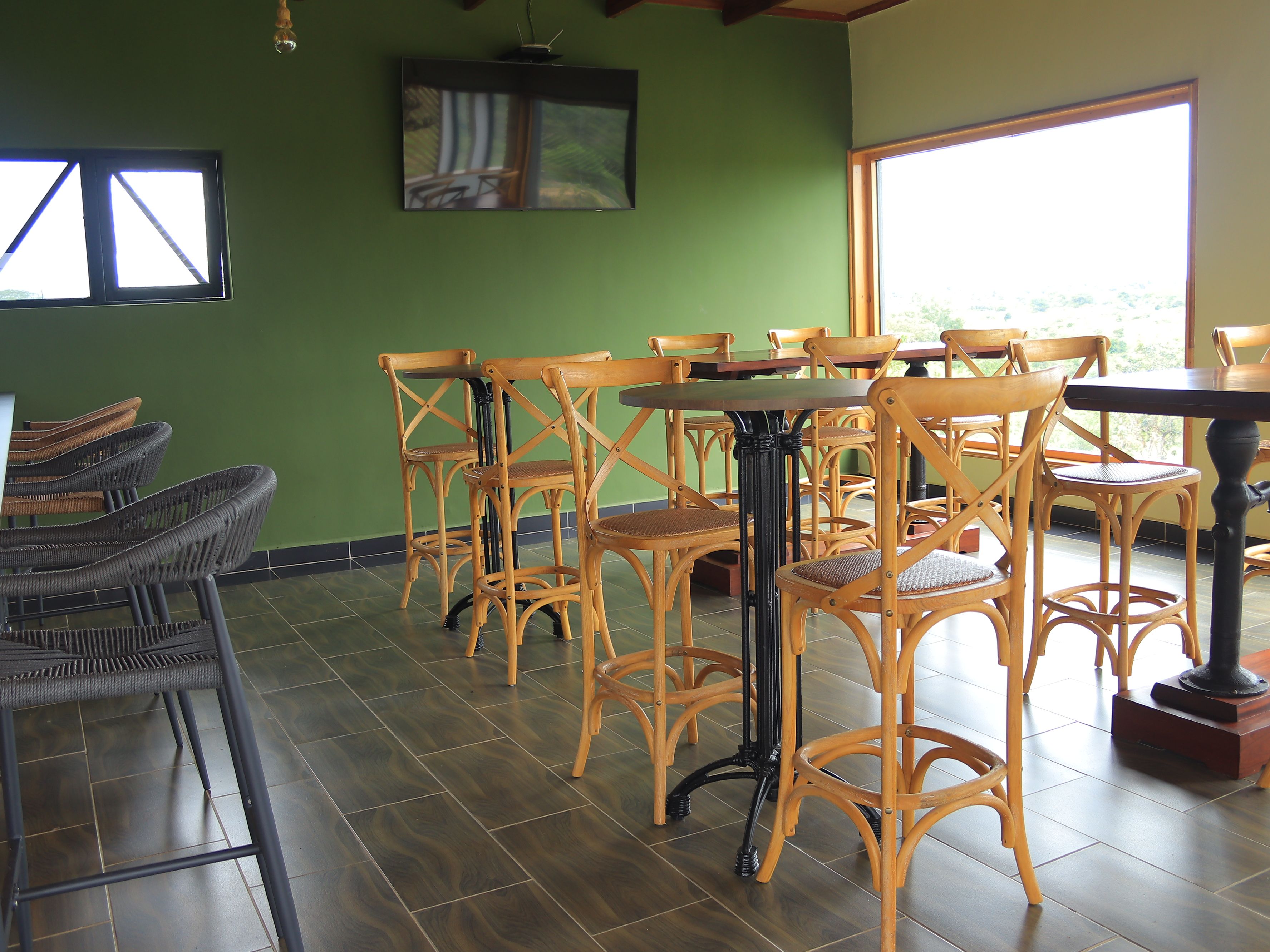 A restaurant interior with wooden chairs and tables, green walls, and a large window.