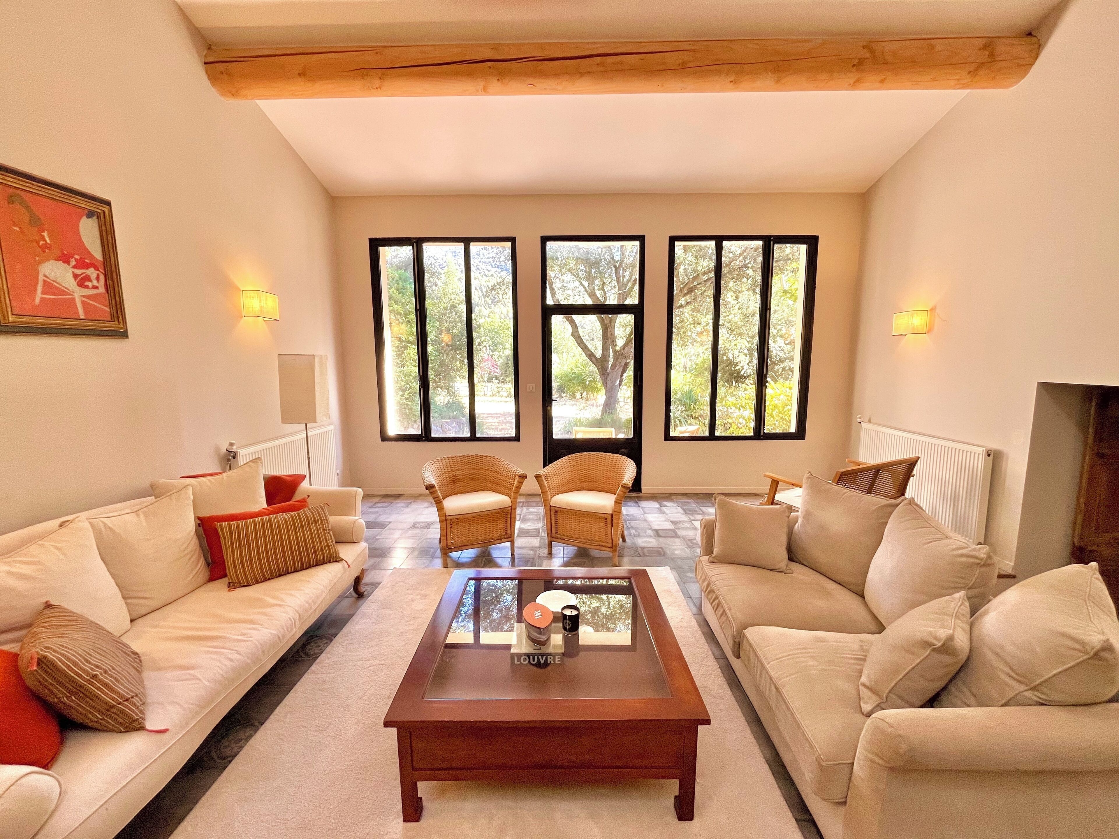 A spacious living room with a large window, a wooden ceiling, and a central coffee table.