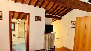 A bedroom with a bed, wooden beams, a wardrobe, and a bathroom visible through an open door. - Casa Nerina (Castiglione d'Orcia)