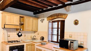 A kitchen with wooden cabinets, a stove, a microwave, and a window with a view. - Casa Nerina (Castiglione d'Orcia)