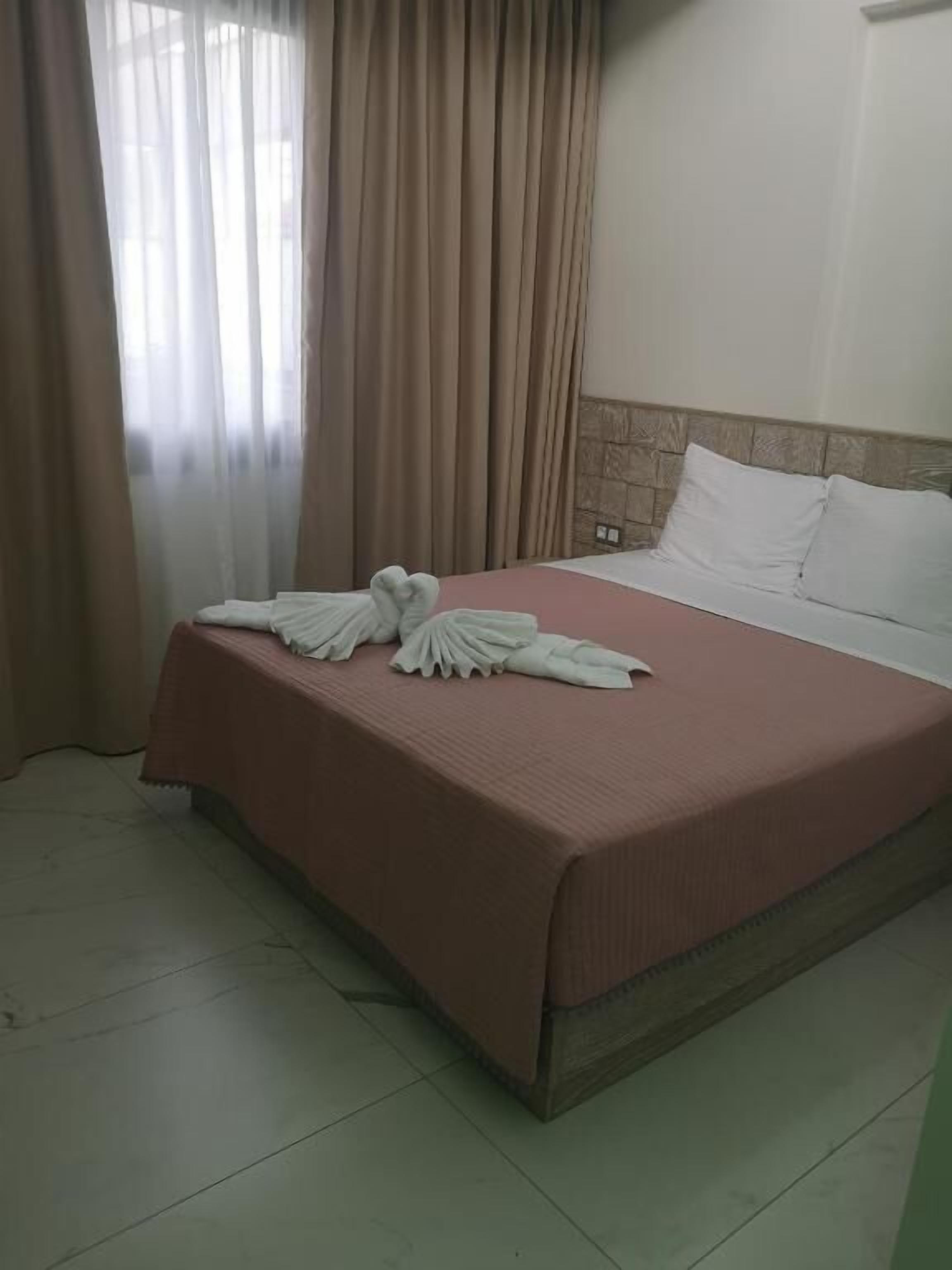 Ein Hotelzimmer mit Bett, beigen Vorhängen und Fliesenboden.