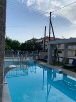 Una piscina con agua cristalina azul, rodeada de sillas de descanso y un muro de piedra.