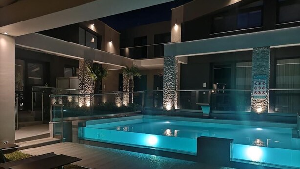 Een modern buitenzwembad met een glazen balustrade, ligbedden en een stenen pilaar.