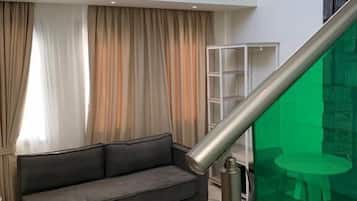 Una sala de estar moderna con un sofá gris, una escalera con barandilla de vidrio y una zona iluminada de color verde.