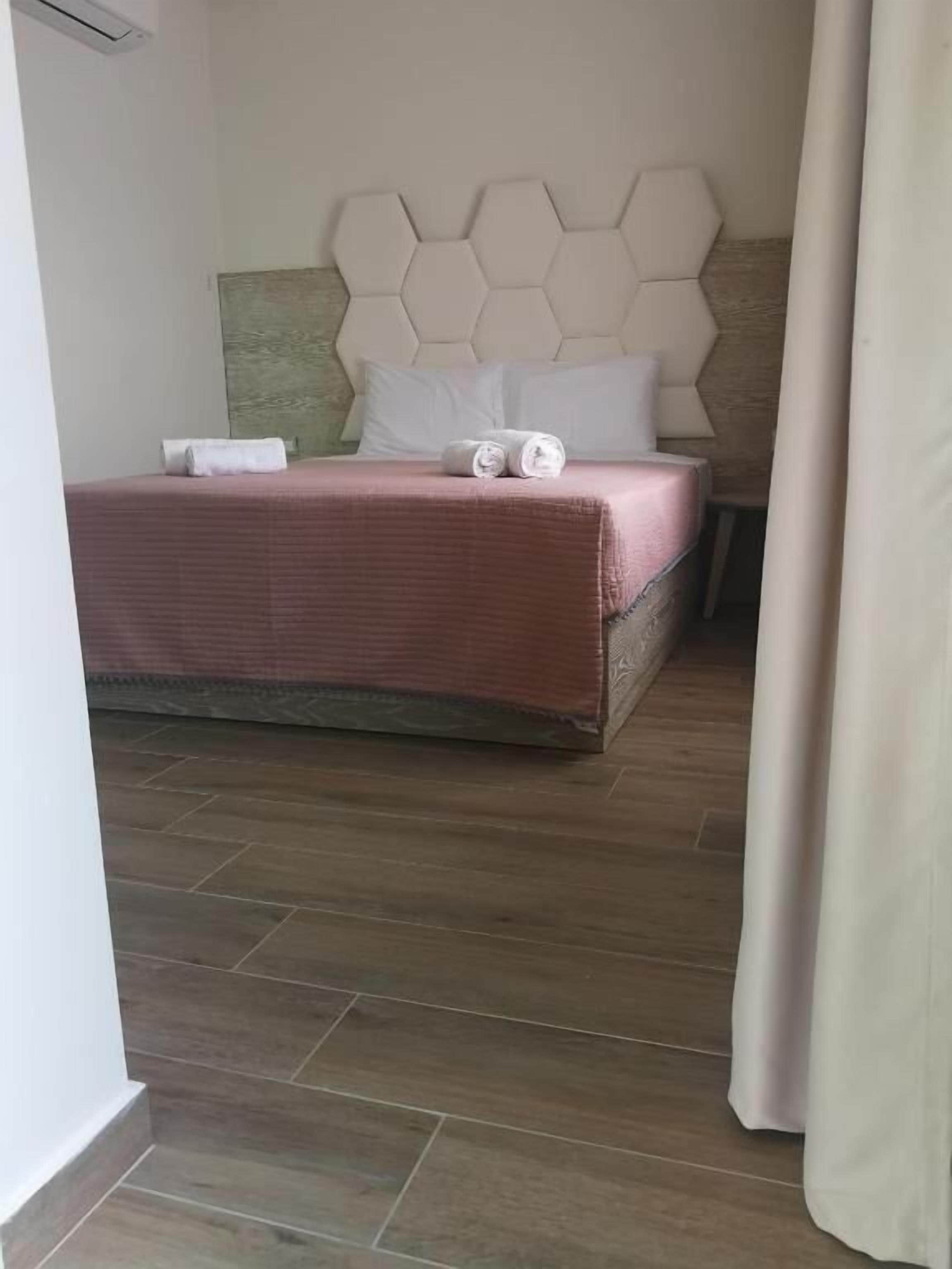 Hotellihuone, jossa on sänky, kuusikulmio-kuvioitu pääty ja puulattia.