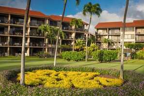 Ein Hotel mit mehreren Etagen, Balkonen und einem gepflegten Garten mit gelben und violetten Blumen.