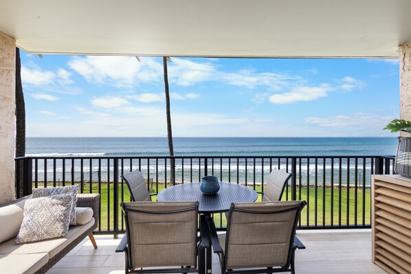 Ein Balkon mit Blick auf das Meer, ein runder Tisch mit Stühlen und eine Couch mit Kissen.