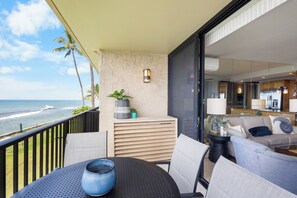 Ein Balkon mit Blick auf den Ozean, eine Sitzecke mit Tisch und eine durch die Glastür sichtbare Küche.