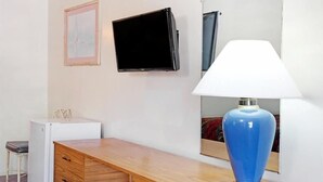 A room with a wooden desk, a white lamp, a flat-screen TV, and a small refrigerator. - Astro Pasadena Hotel (Pasadena)