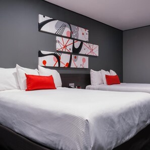 Hotellihuone, jossa on kaksi sänkyä, valkoiset vuodevaatteet, punaiset tyynyt ja abstrakti taideteos seinällä.
