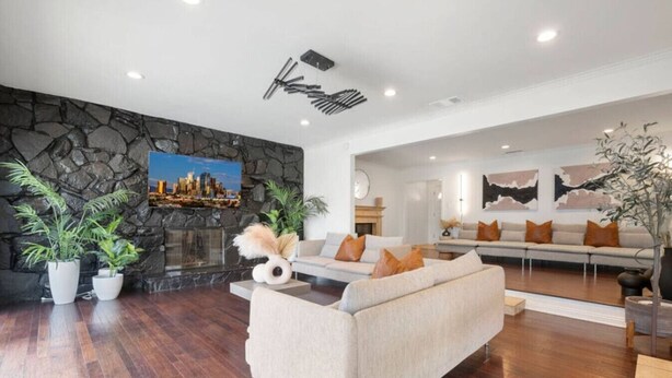 A modern living room with a stone accent wall, a fireplace, a sofa set, and a cityscape painting. - Blue Haven | Solar Pool Heat + Parking + Billiards (Long Beach)