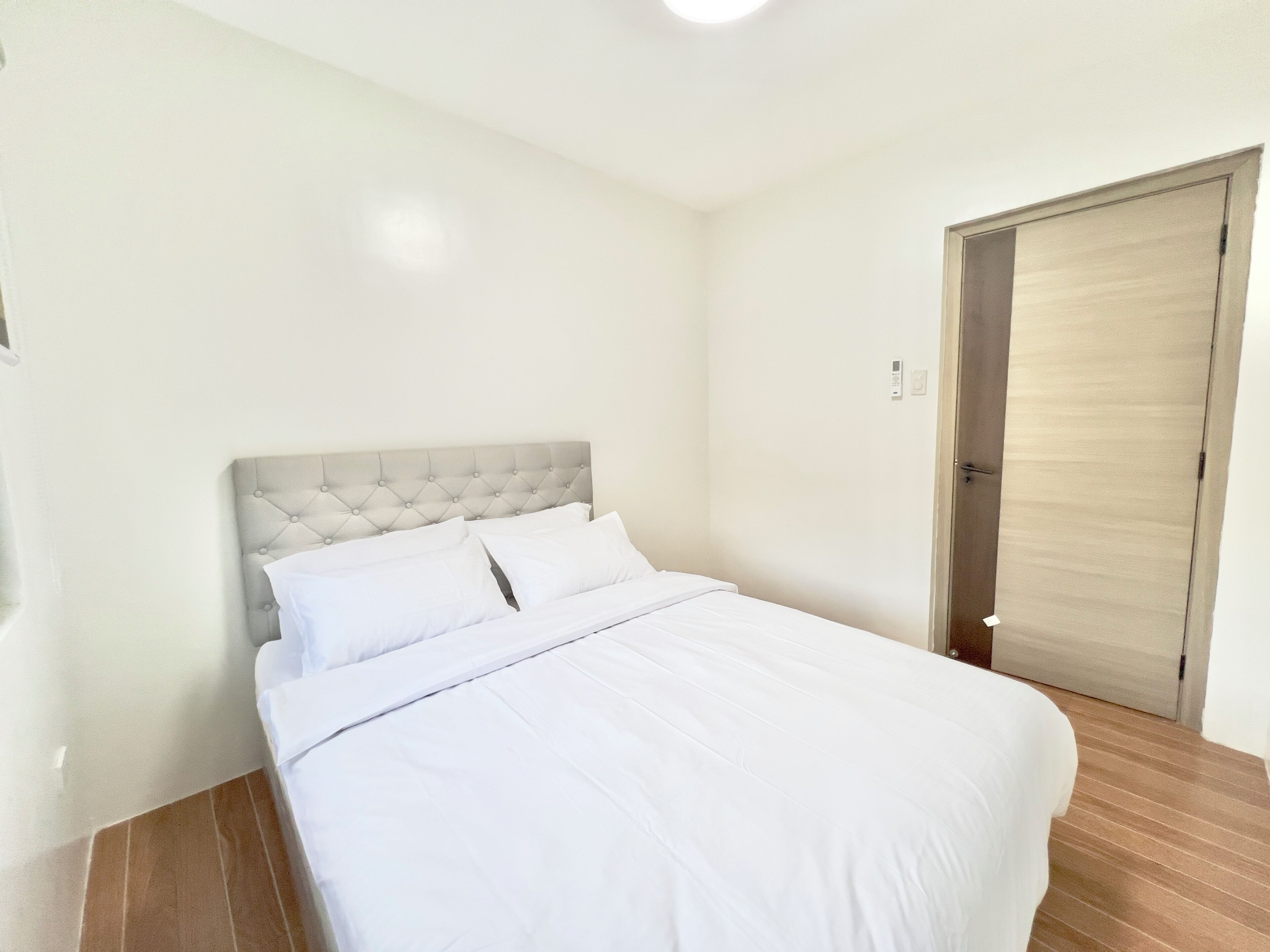 A bedroom with a bed, a wooden door, and a light switch on the wall.